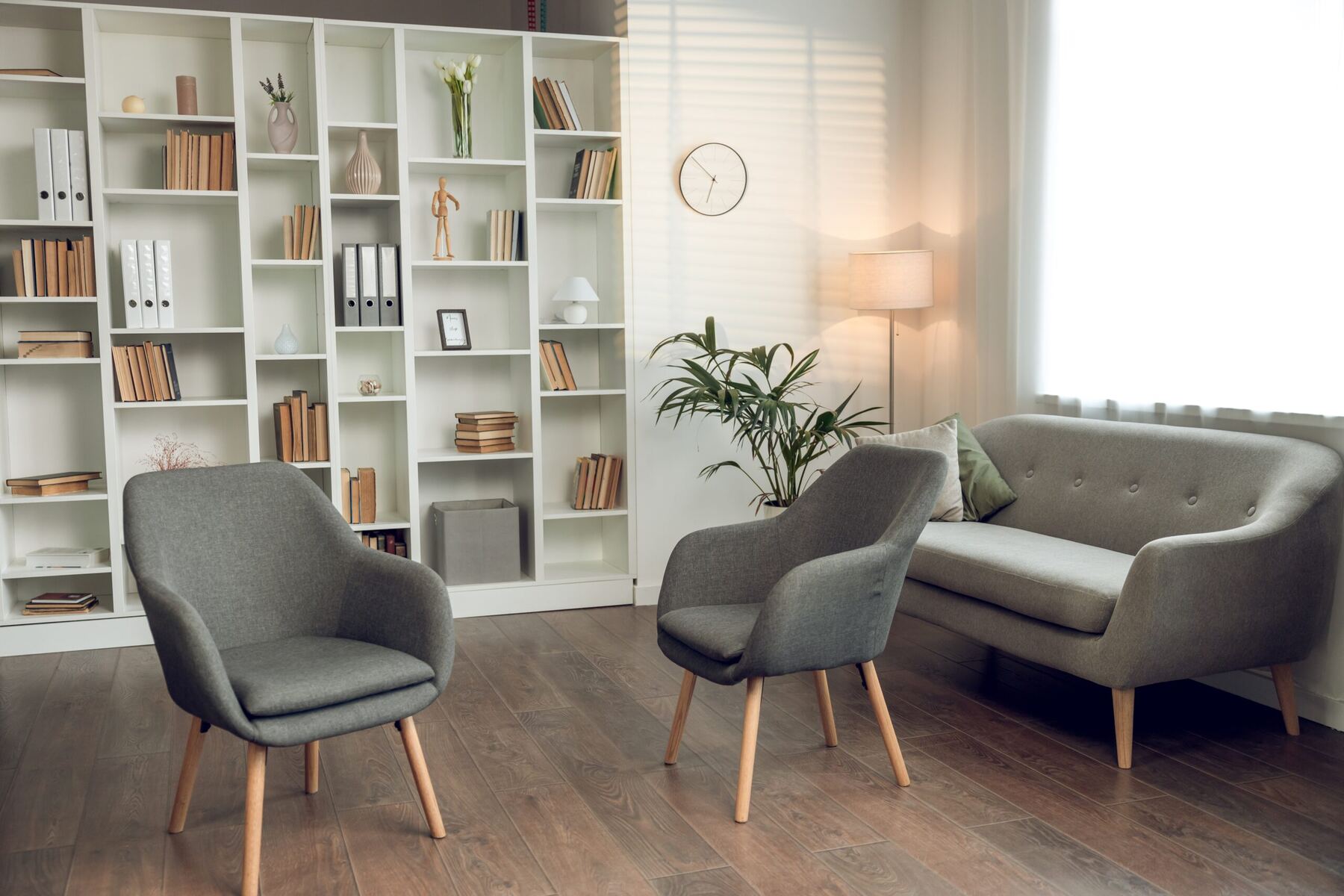 A calm therapy room with two armchairs, a sofa, bookshelves and soft window light