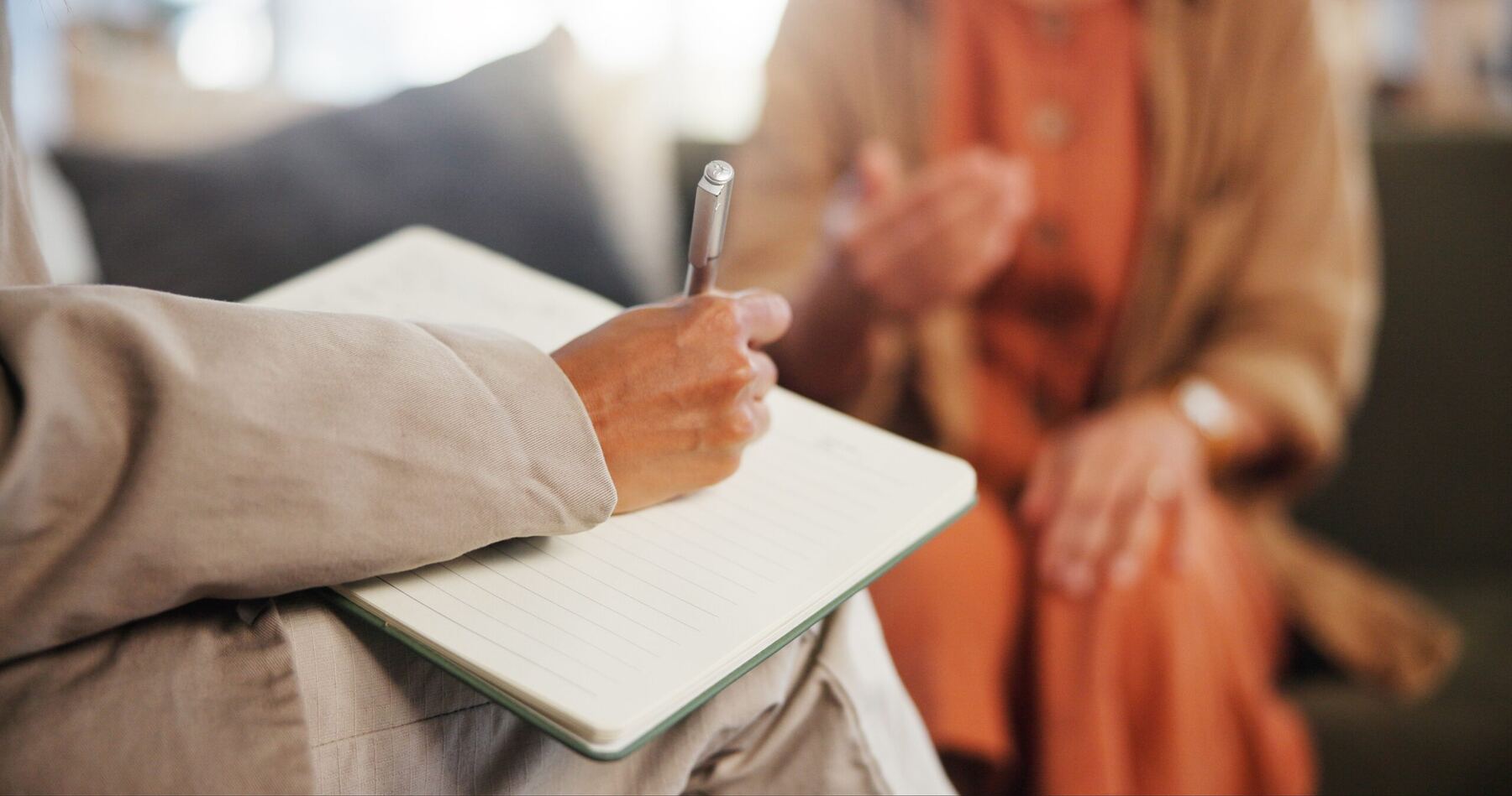 A therapist writing notes in a notebook while listening to a client